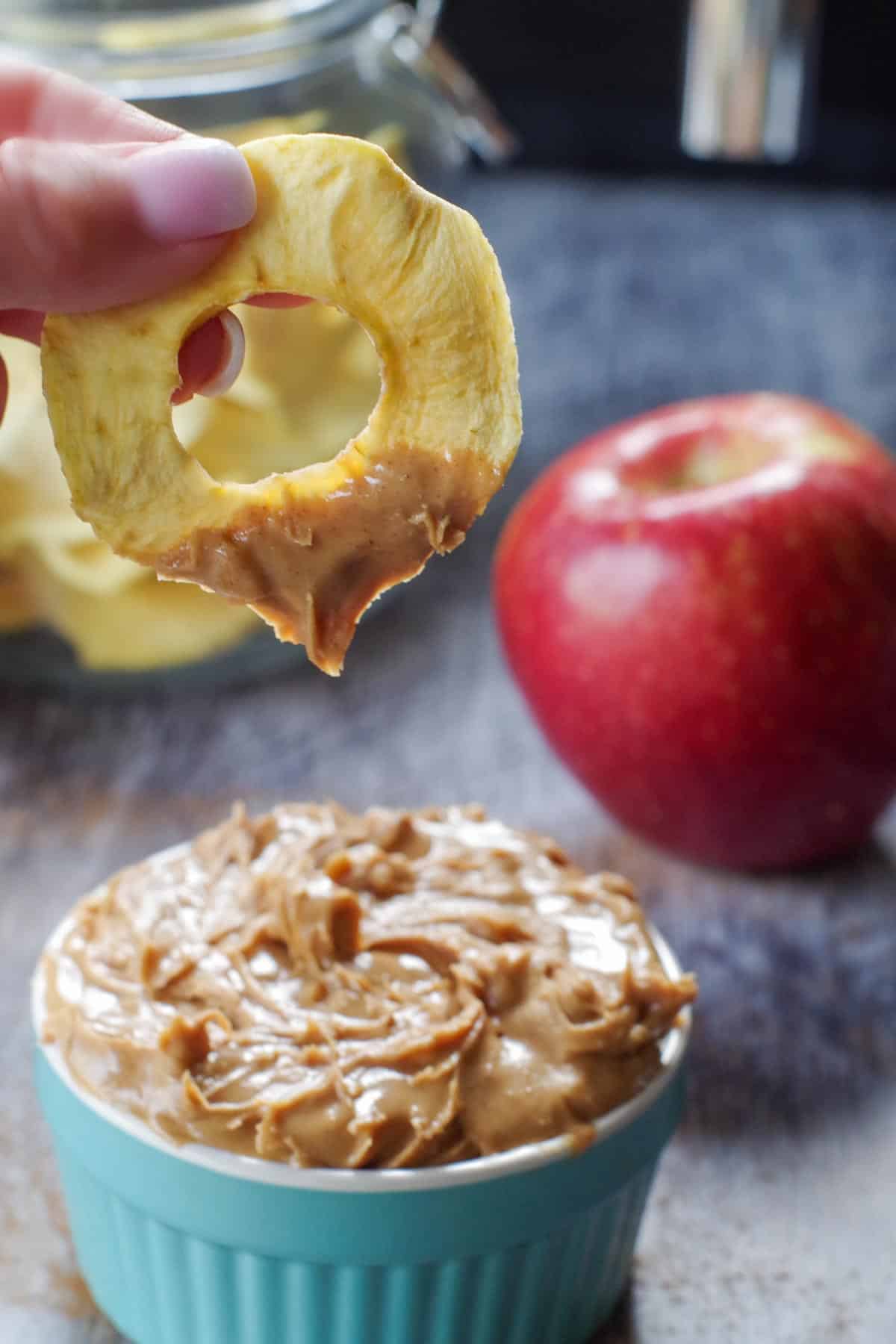 air fryer dehydrated apple being dipped into a small container of peanut butter