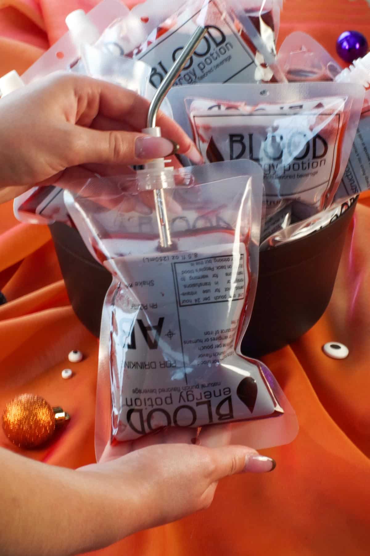 Halloween blood bag with a straw in it and more blood bags in a cauldron in the background