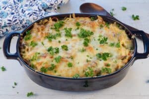 cooked turkey tetrazzini in casserole dish with wooden spoon on the side and blue patterned oven mitts in the background