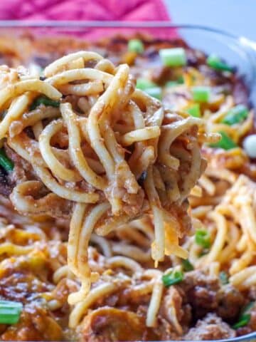 Million Dollar Spaghetti Casserole being held up on a spoon over glass casserole dish