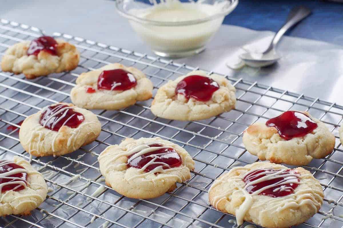 White Chocolate raspberry cookies on a wire cooling rack, being drizzled with white chocolate
