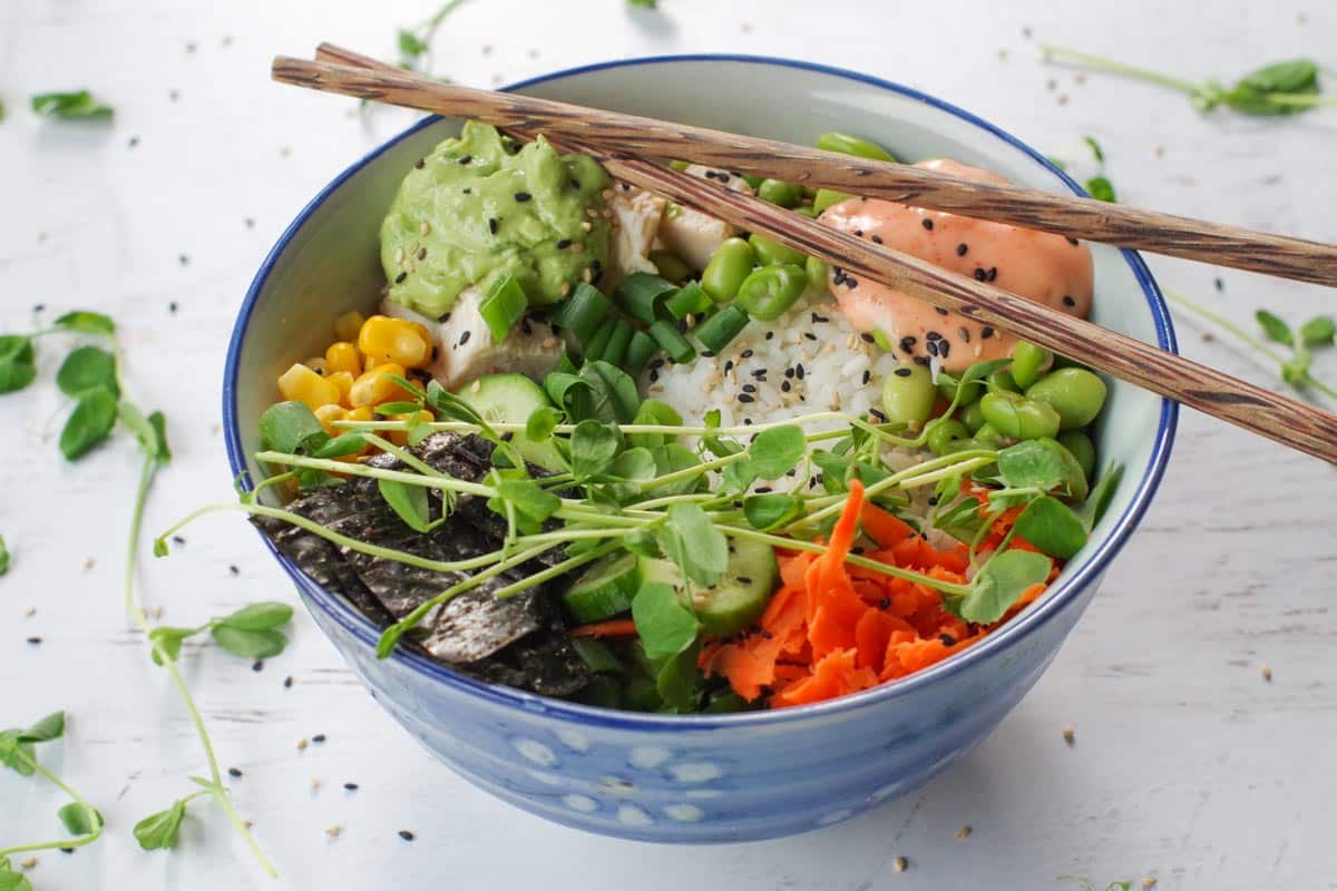 chicken poke bowl with chopsticks laying over the bowl and pea shoots strewn around bowl.