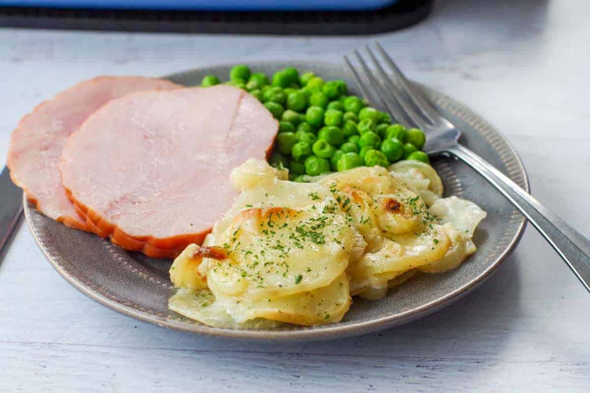 scalloped potatoes on a plate with ham and peas