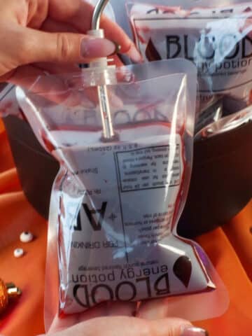 Halloween blood bag with a straw in it and more blood bags in a cauldron in the background