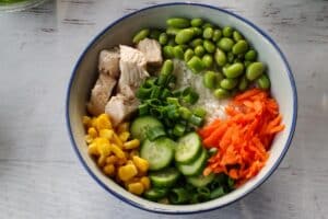 carrots, corn, cucumber, green onion and edamame added to bowl with rice and chicken
