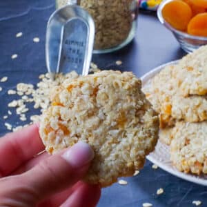 hand holding one Oatmeal Apricot cookie in front of a plate of more Apricot Oatmeal cookies