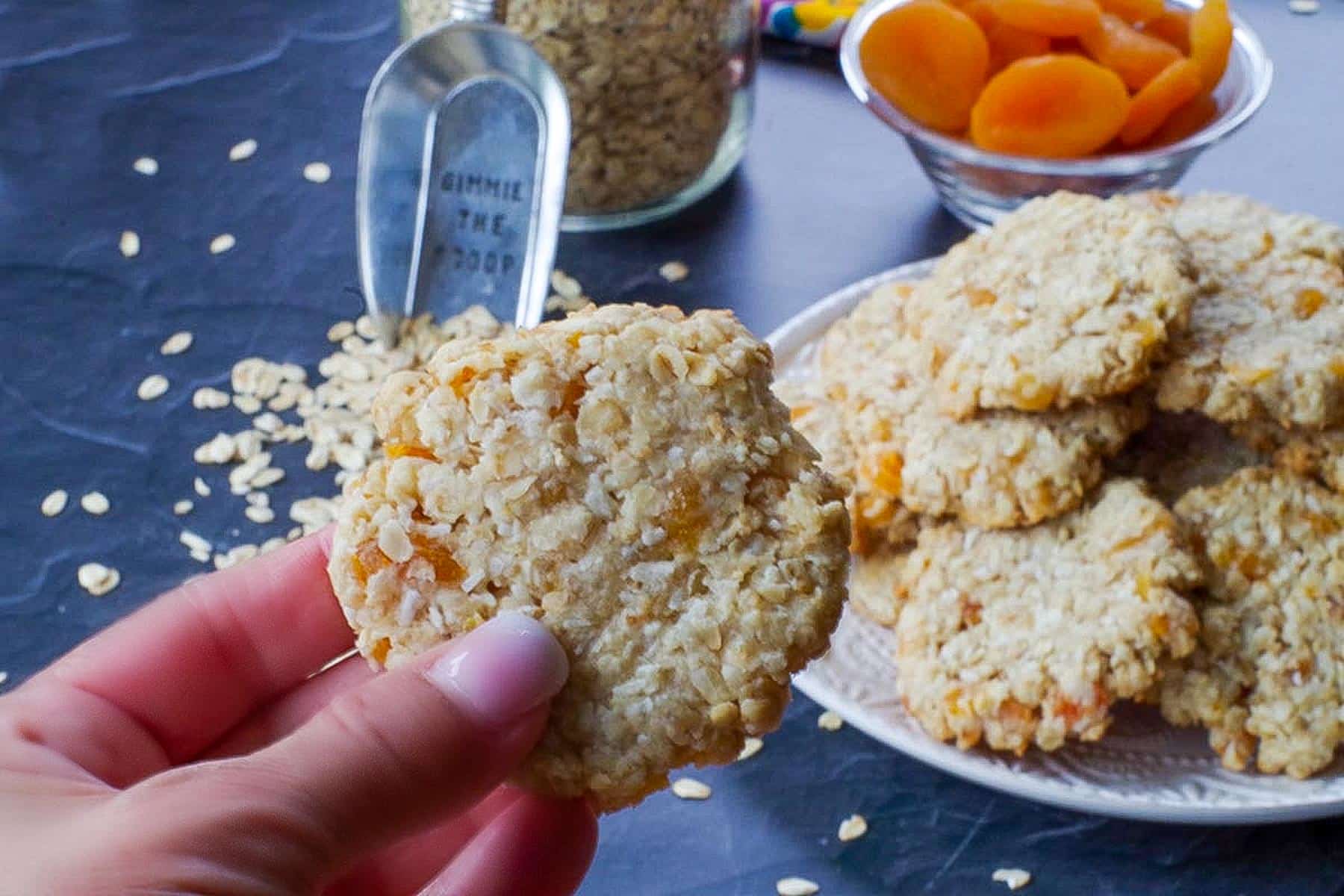 hand holding one Oatmeal Apricot cookie in front of a plate of more Apricot Oatmeal cookies