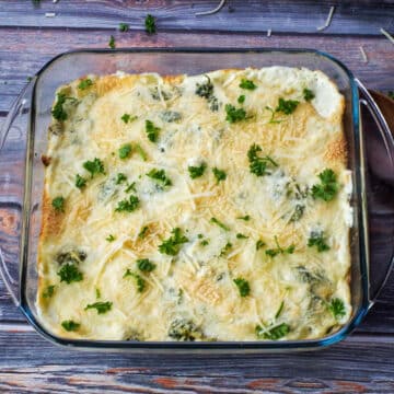Spinach Artichoke casserole in glass pan on faux wood surface