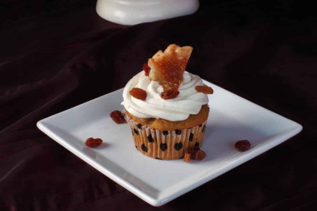 single butter tart cupcake on a white plate with raisins strewn around