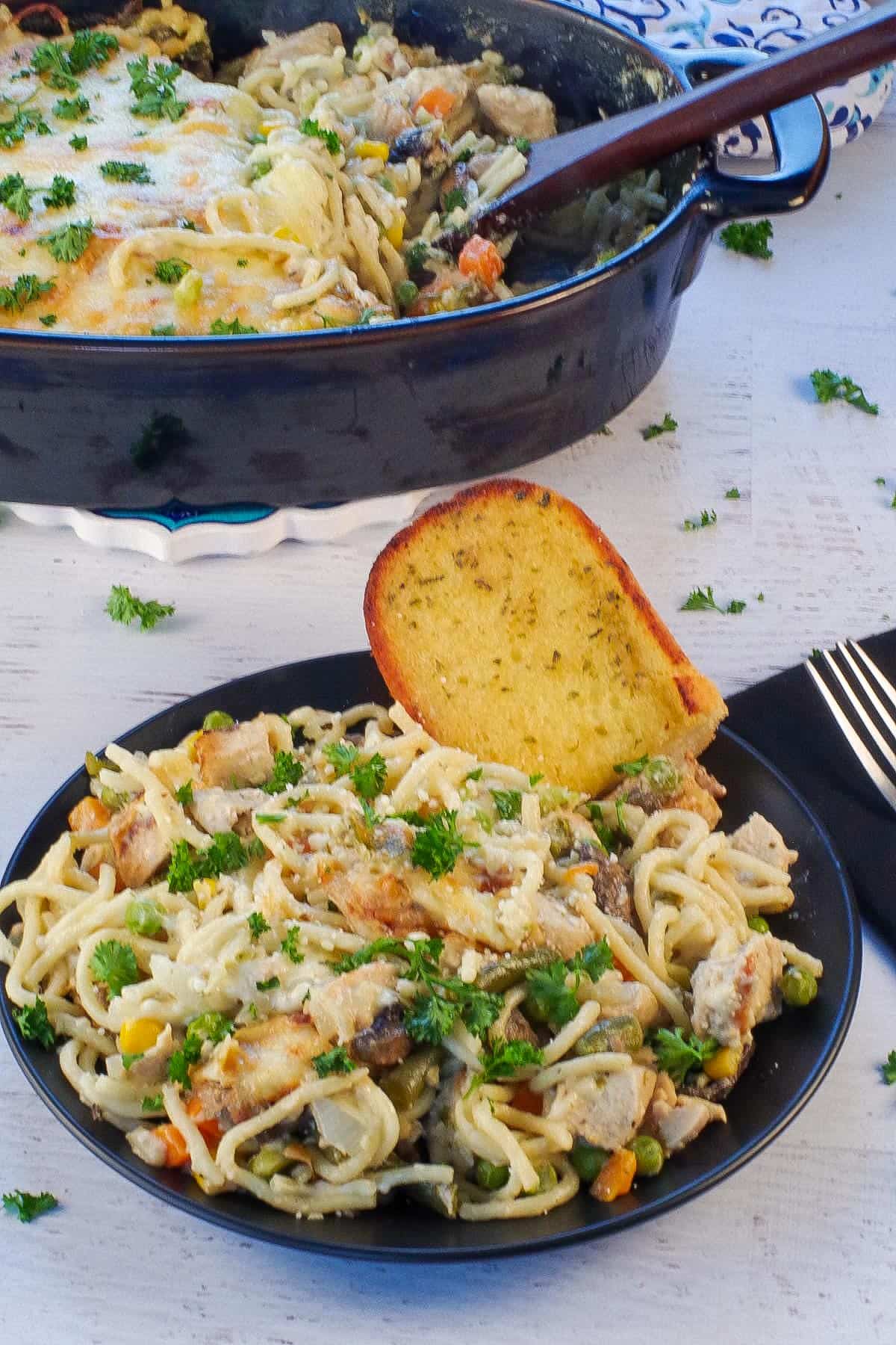 turkey tetrazzini on a black plate with a piece of garlic toast, with more in casserole dish in background