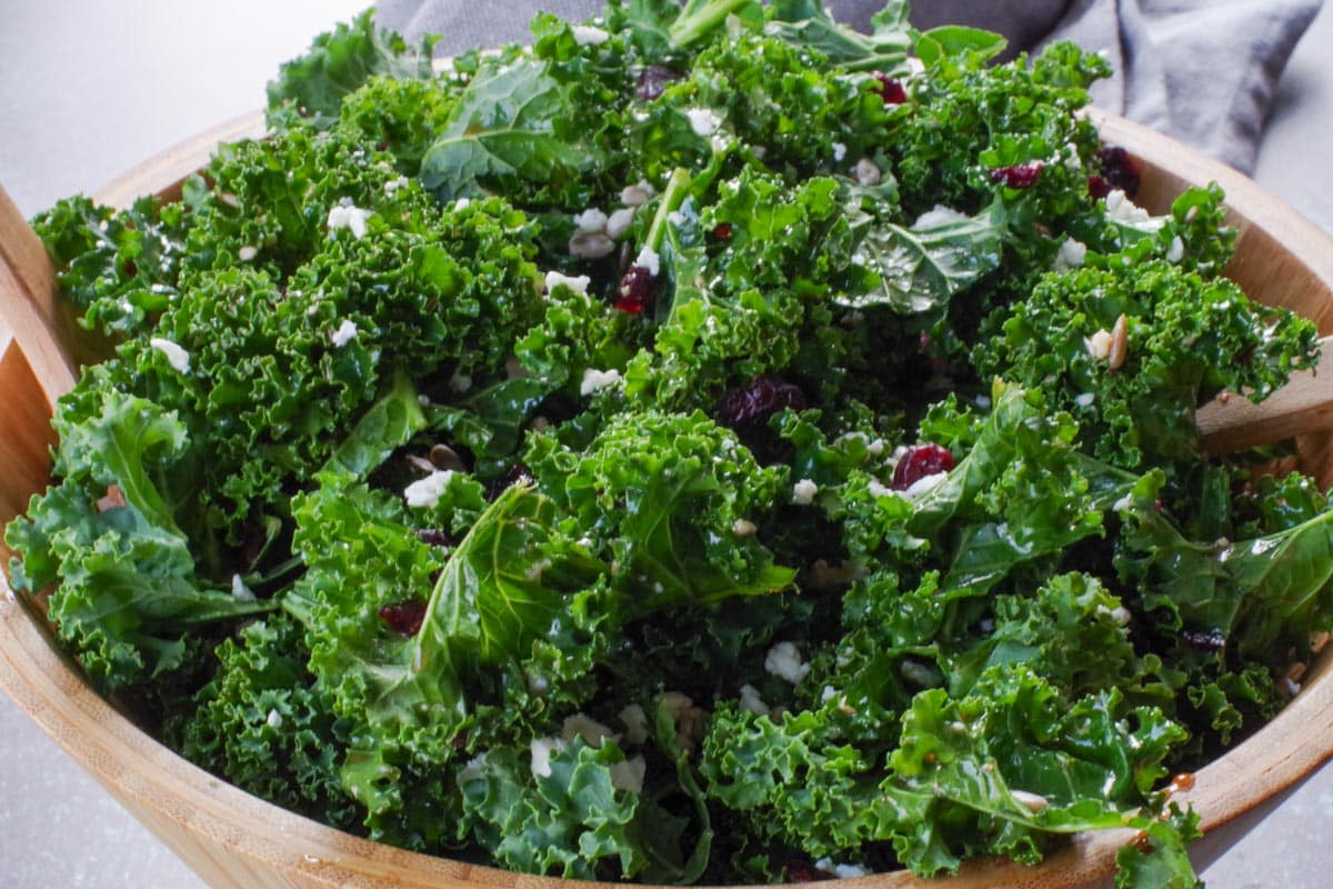 close up shot of kale salad in wooden bowl with wooden utensils