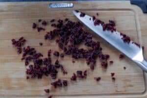 dried cranberries being chopped with a sharp knife on a wooden cutting board