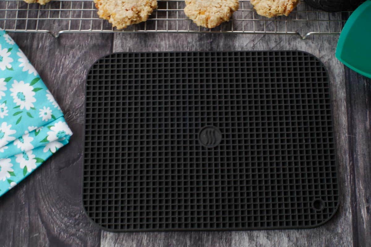 large black silicone trivet on faux wood surface with cookies in background