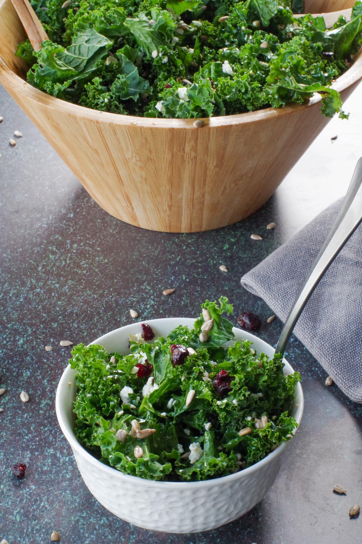 kale salad in small white bowl in front of more salad in large wooden bowl in background