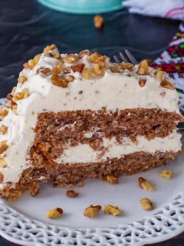Slice Ukrainian Walnut Torte on a white plate with a whole cake in background