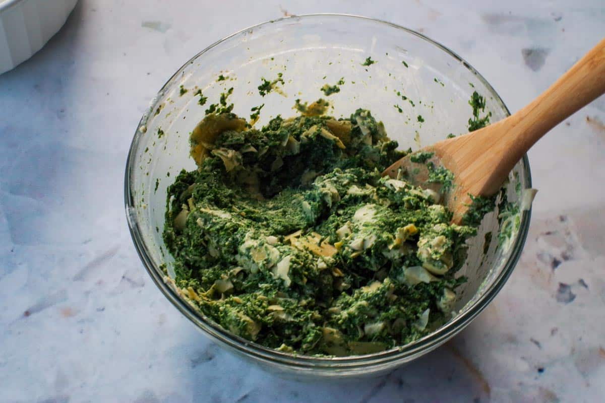 spinach artichoke mixture in large glass bowl with wooden spoon
