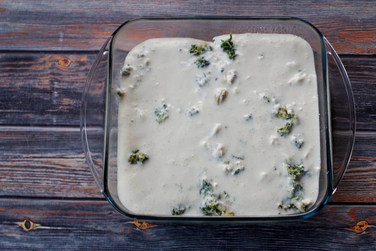 cream cheese mixture poured over spinach artichoke mixture in square glass baking dish