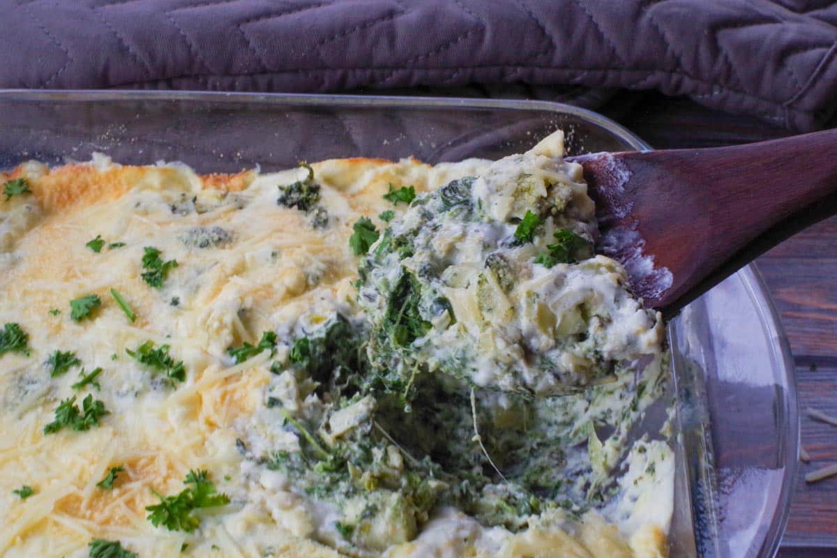 spinach artichoke casserole with dark wooden spoon scooping out a portion