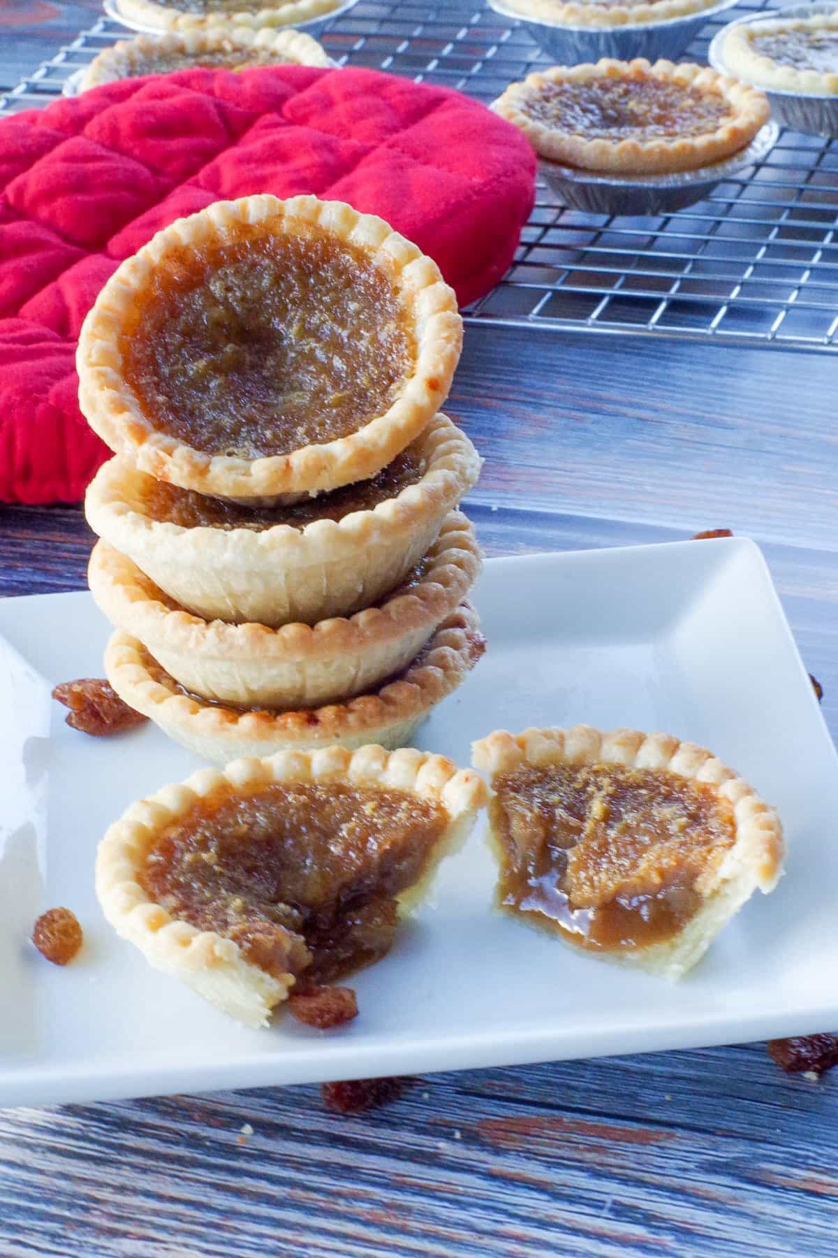 4 butter tarts stacked on a white plate, with a butter tart split in half in front of the stack