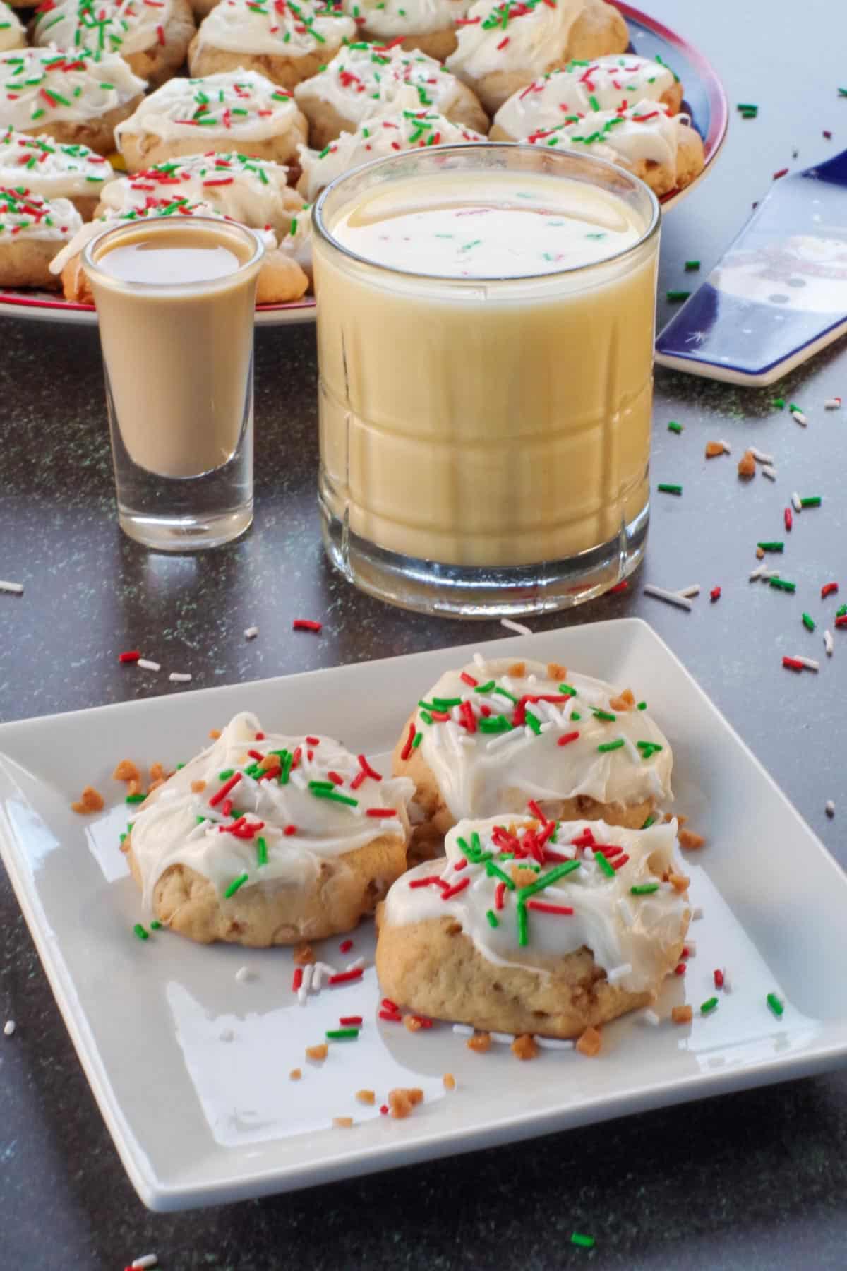 3 eggnog and baileys irish cream cookies on a white plate with a glass of eggnog and a shot of baileys in the background