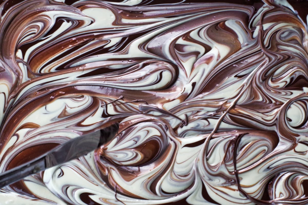 melted chocolate being marbled with knife on sheet pan