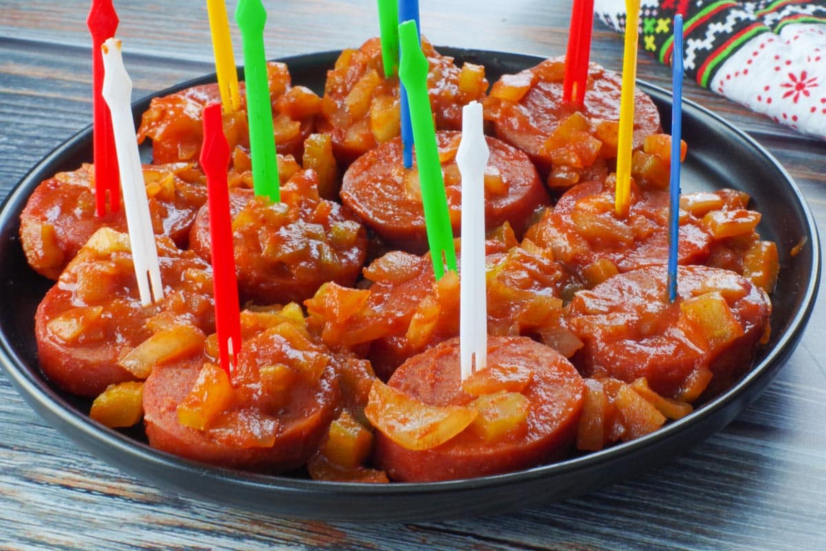 slow cooker kielbasa appetizer with colorful plastic skewers, on a black round plate