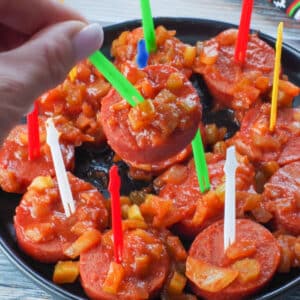 slow cooker kielbasa appetizer on a green plastic skewer being picked up