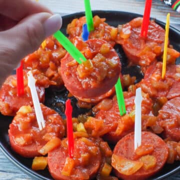 slow cooker kielbasa appetizer on a green plastic skewer being picked up