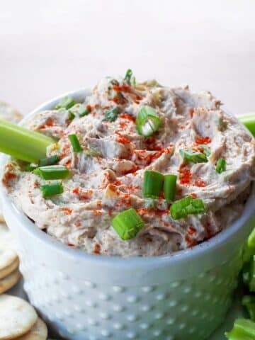 tuna dip in white container on a tray with crackers and celery with a piece of celery sitting in the dip
