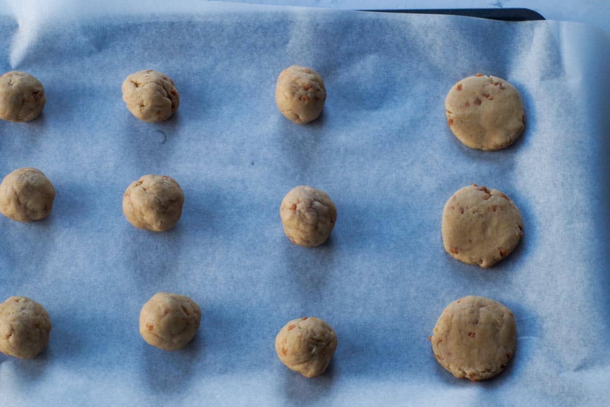 cookie dough rolled into balls on a parchment covered baking sheet, with some flattened