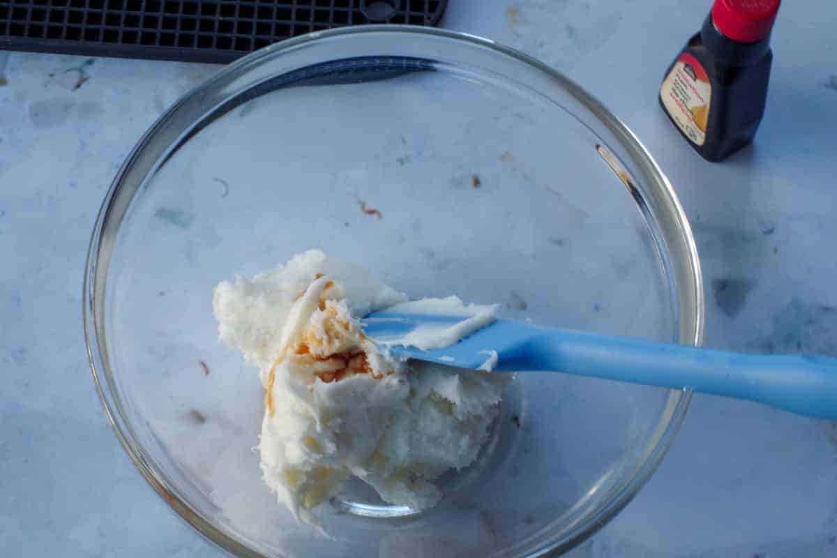 rum extract being mixed into frosting in a glass bowl, with a blue spatula