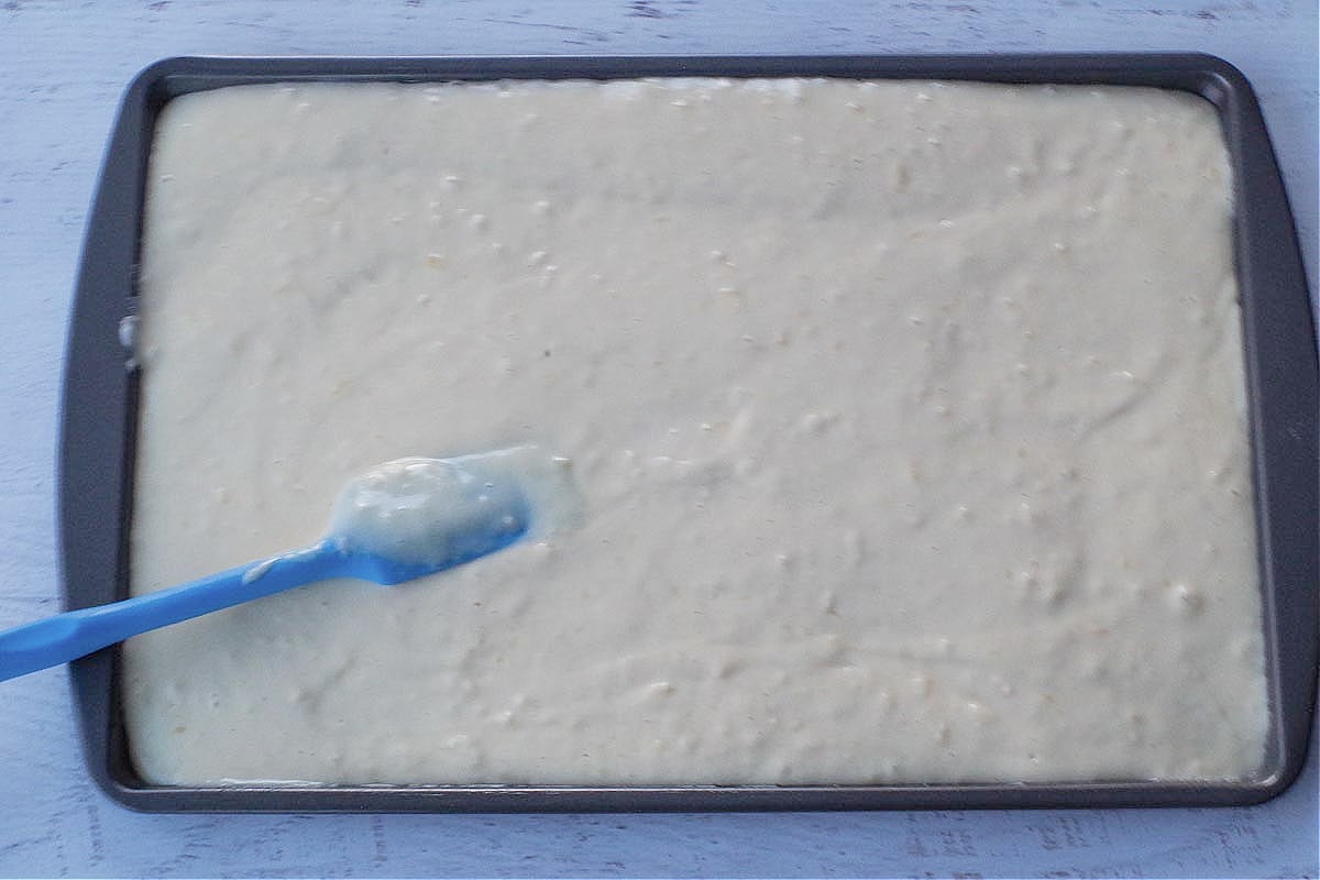 pancake batter poured onto sheet pan with blue spatula spreading it