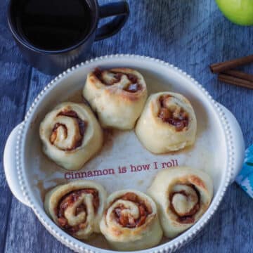 6 Apple Pie 2 Ingredient Dough Cinnamon rolls in a white baking dish, with the words, " cinnamon is how I roll" printed in the middle of the dish