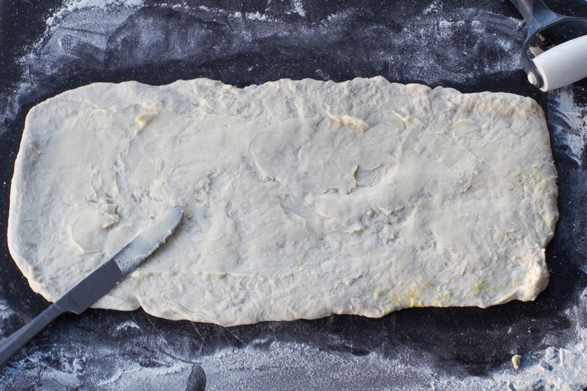 dough rolled out into rectangle on large cutting board, with butter spread on it