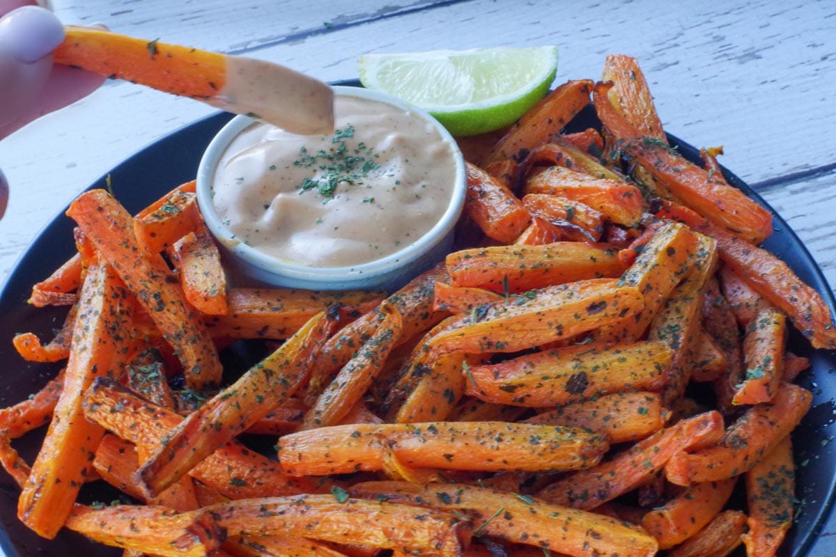 carrot fry being dipped into dip over a plate of more carrot fries