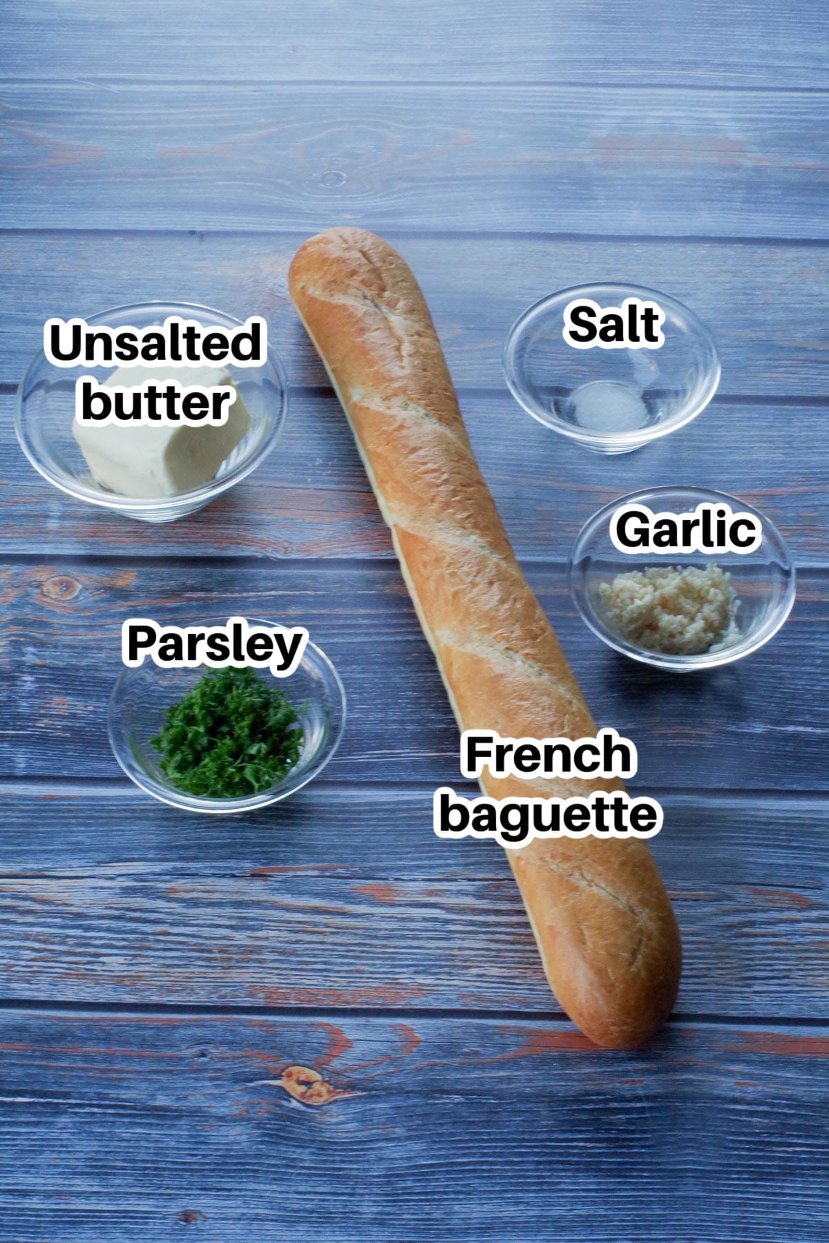ingredients in garlic bread baguette (bread directly on the surface and other ingredients in glass bowls) on faux blue wooden surface
