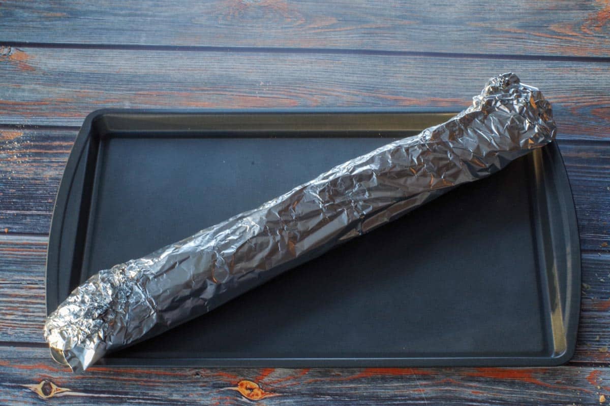 baguette tightly wrapped in foil on baking sheet