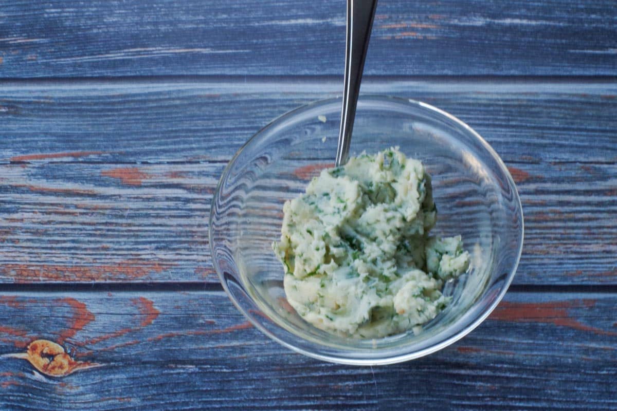 butter, parsley, garlic and salt mixed together in glass bowl, with a spoon