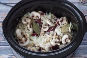 uncooked beef, mushrooms onions and bay leaves in a crockpot