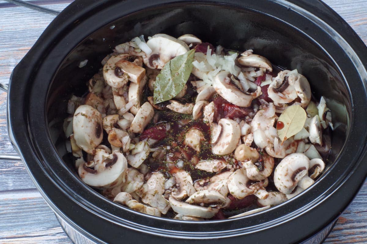 meat and mushroom mixture with liquid herb mixture poured on top, in slow cooker