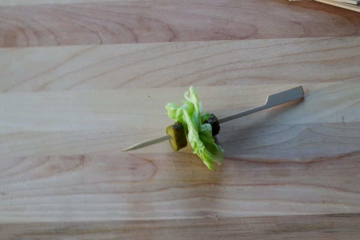 a skewer with pickles and lettuce on a wooden cutting board