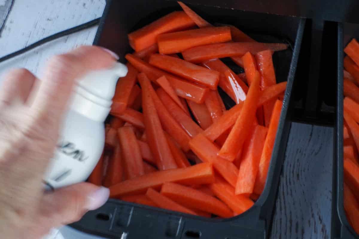 raw carrot fries being sprayed with oil