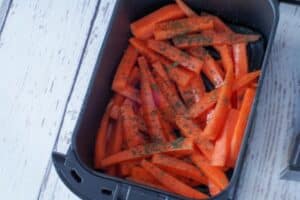 raw carrot fries in air fryer drawer sprinkled with spices