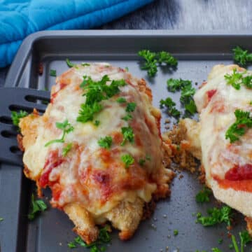 2 chicken parmesan breasts on a sheet pan with a blue oven mitt in the background