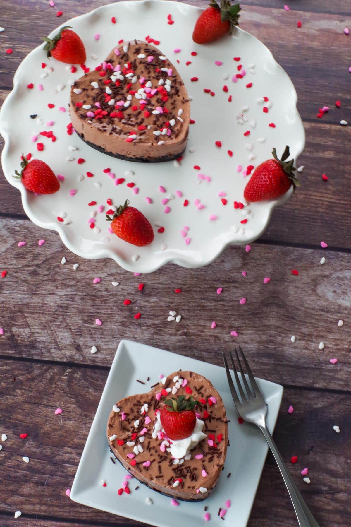 a heart-shaped Valentine's day cheesecake on a white plate with a another one on a white platter in the background