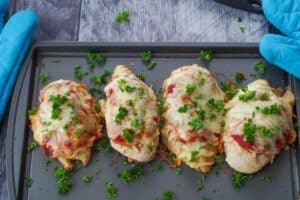 4 one pan chicken parmesan garnished with parsley on a sheet pan with blue oven mitts