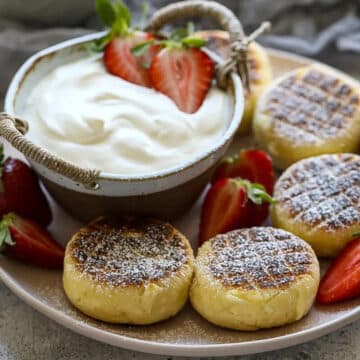 4 syrniki pancakes on a plate with yogurt and strawberries in the middle