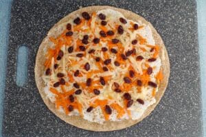 tortilla with cream cheese, cinnamon, shredded apple, shredded carrot and raisins on a cutting board