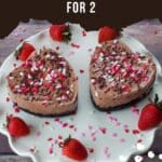 2 Valentine's Day Chocolate Strawberry Cheesecakes on a white cake platter with strawberries and heart sprinkles