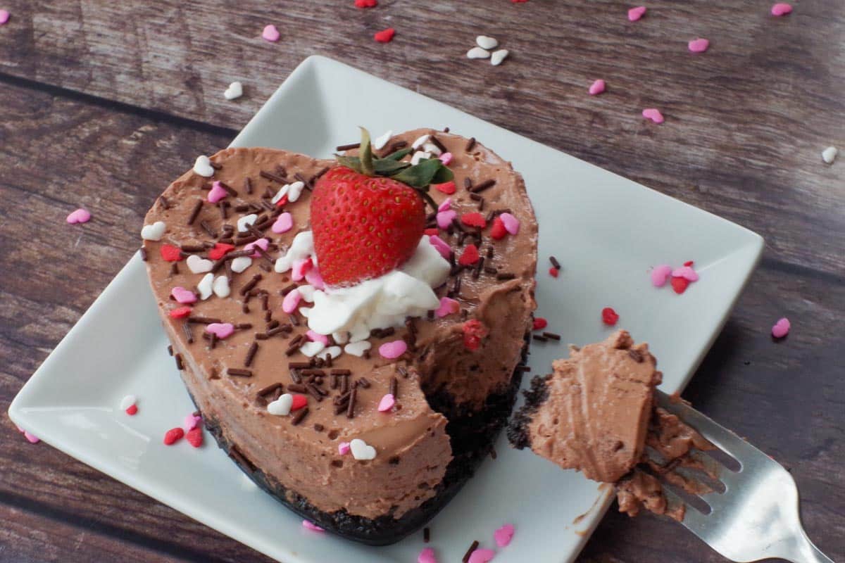 Valentine's Day strawberry chocolate cheesecake on a white plate with a bite sized piece on a fork
